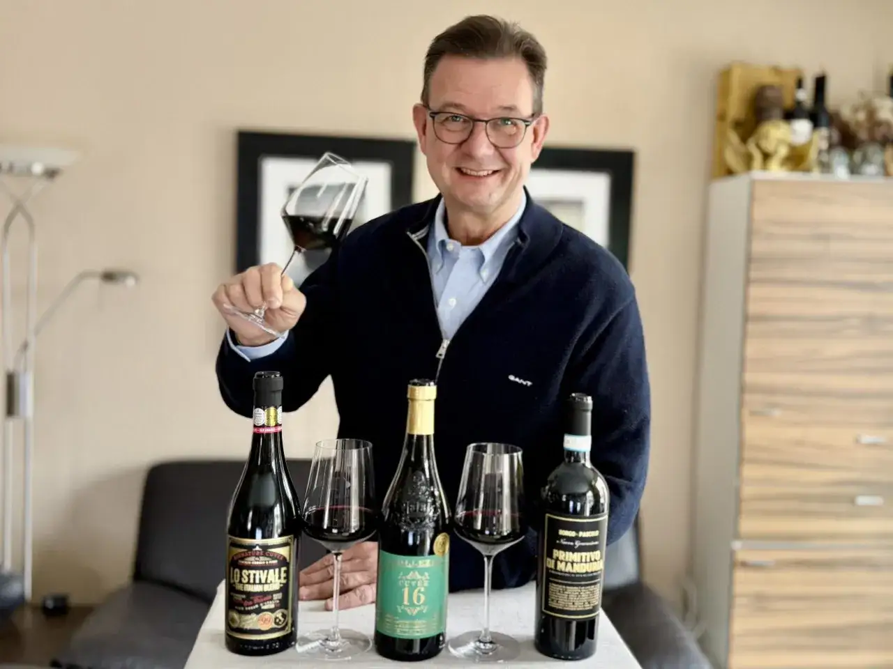 Luca Maroni präsentiert stolz drei Flaschen Rotwein und ein Glas.