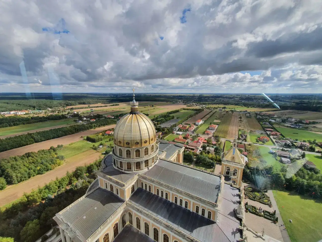 Bazylika w Licheniu z lotu ptaka. Widok na złotą kopułę i otaczający krajobraz. Planujesz wizytę? Sprawdź licheń cennik.