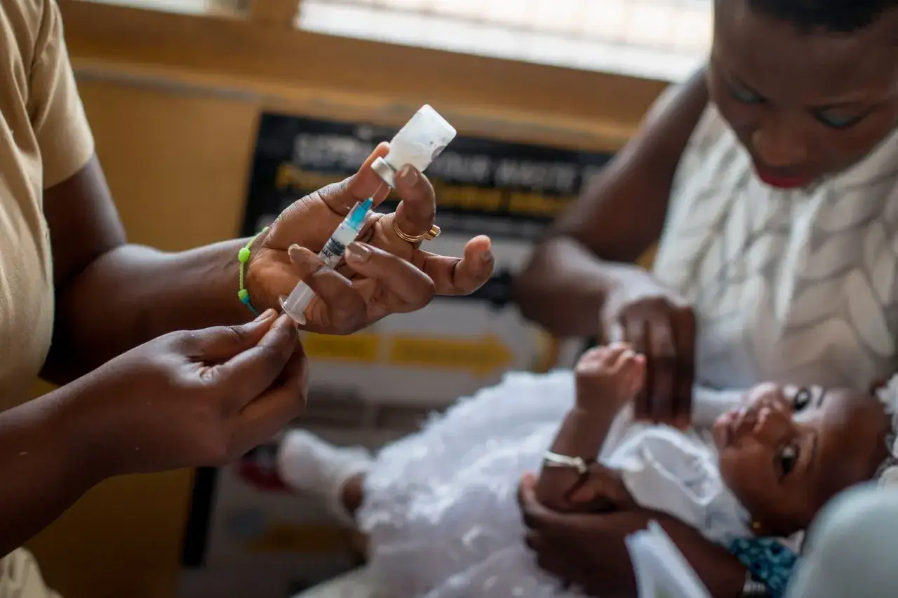 En sjukvårdare förbereder en spruta med malaria vaccin för ett litet barn.