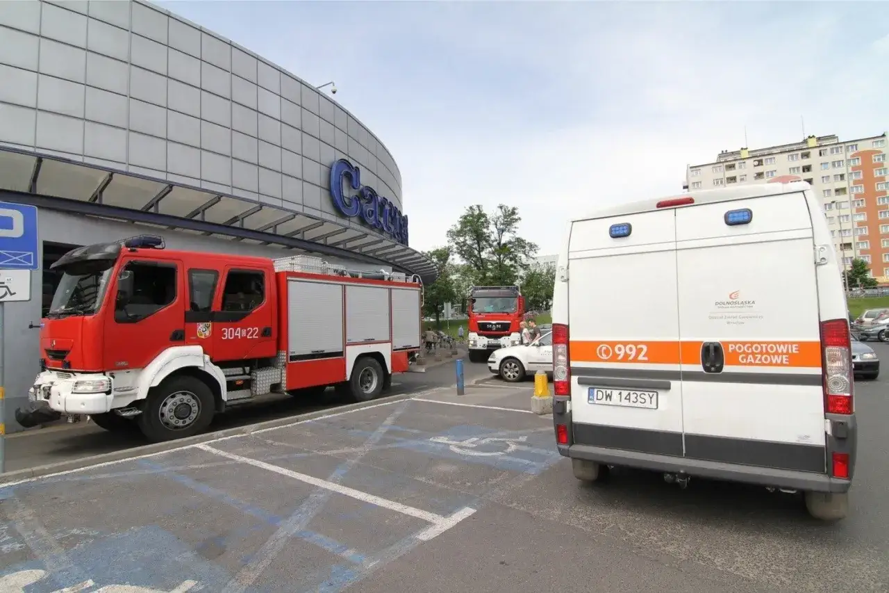 Awaria gazu w domu? Zgłoś pod numer 992. Widoczny wóz pogotowia gazowego i straży pożarnej przed budynkiem.