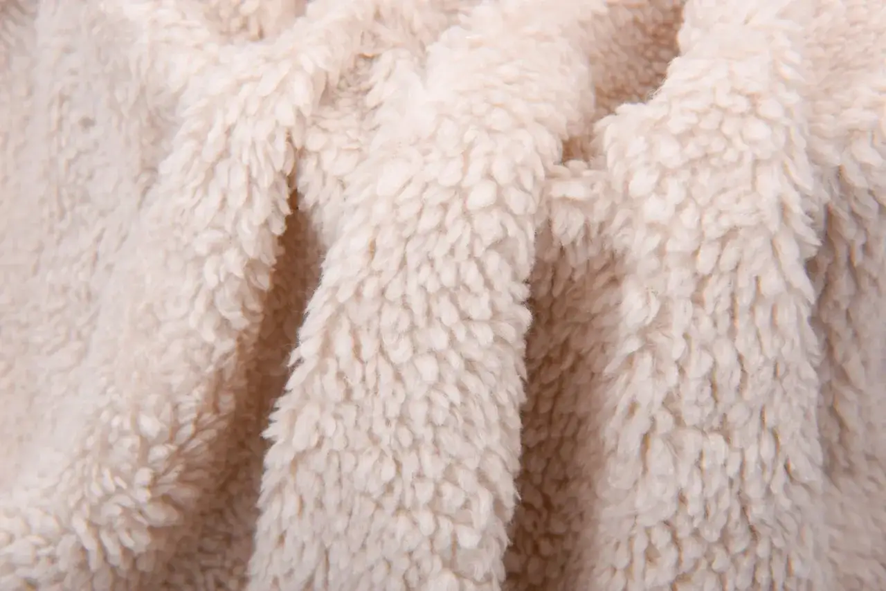 Close-up of fluffy, cream-colored sherpa fleece. This cozy material is often vegan, offering warmth without animal products.