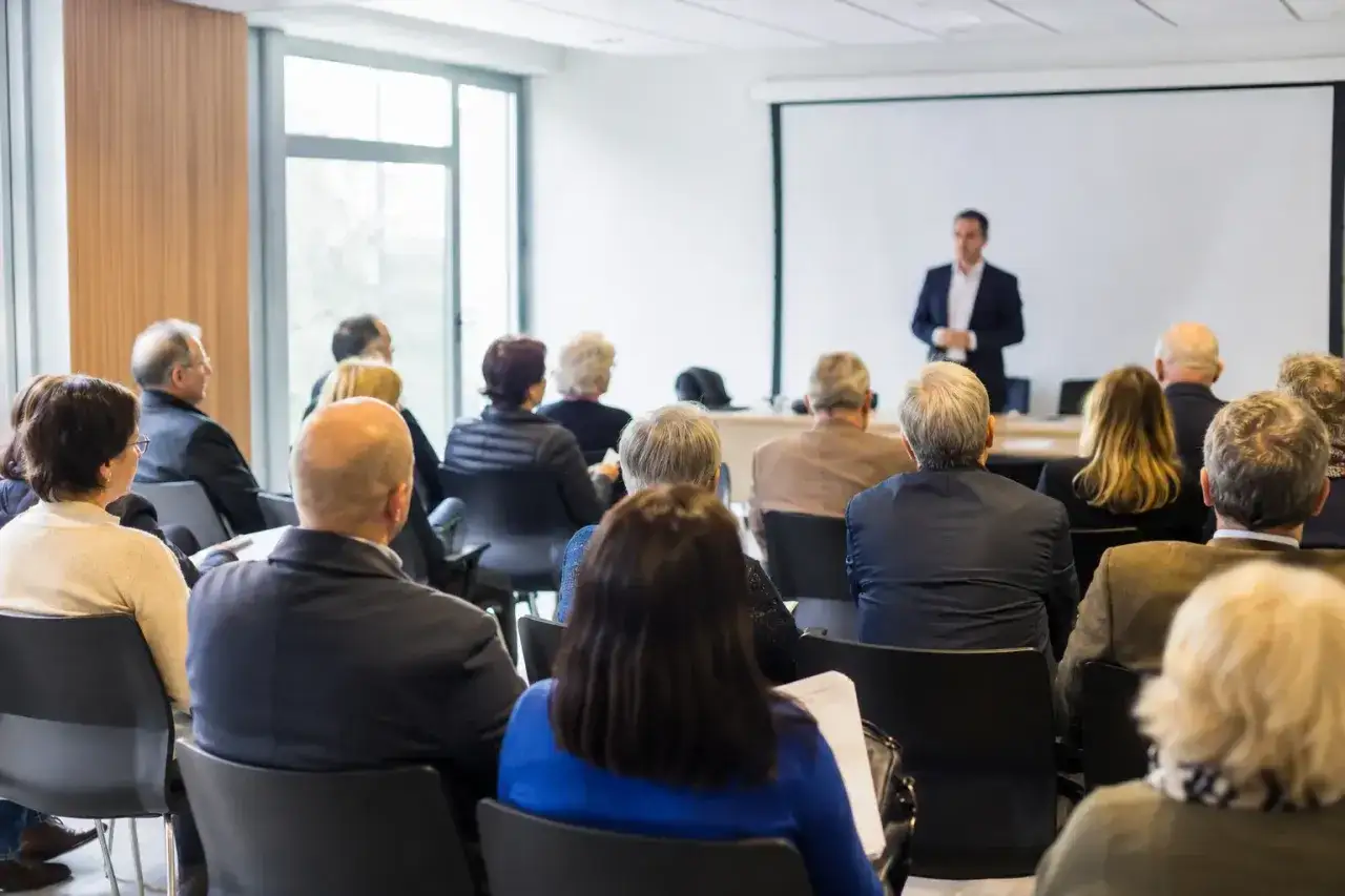 Conférence sur comment changer de syndic en 5 étapes. Un orateur s'adresse à un public assis dans une salle de réunion.