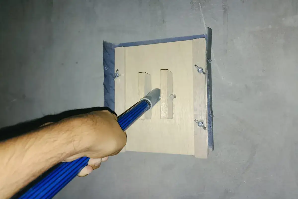 Mano lijando paredes para pintar con una herramienta de madera y metal.
