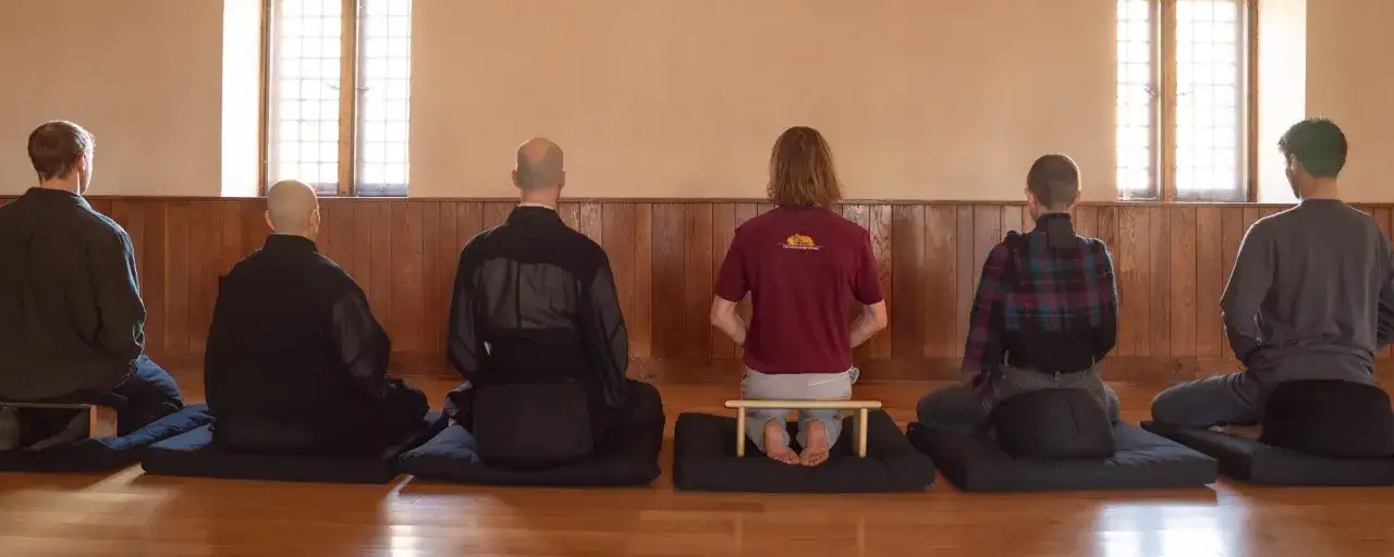 Sju personer sitter i meditation, en del i munkkl&auml;der, andra i vardagskl&auml;der. En tyst stund av buddhism och inre ro.