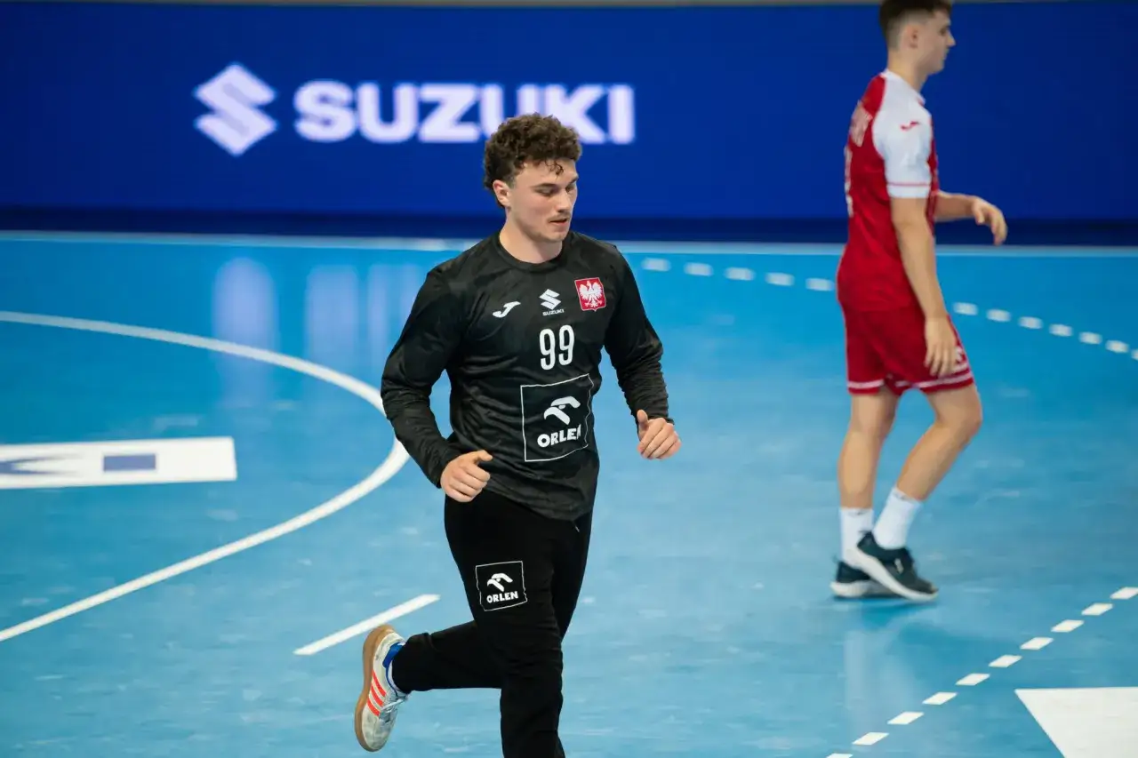 Jakub Wysocki w czarnej koszulce z numerem 99 i herbem Polski biegnie po niebieskiej hali sportowej.