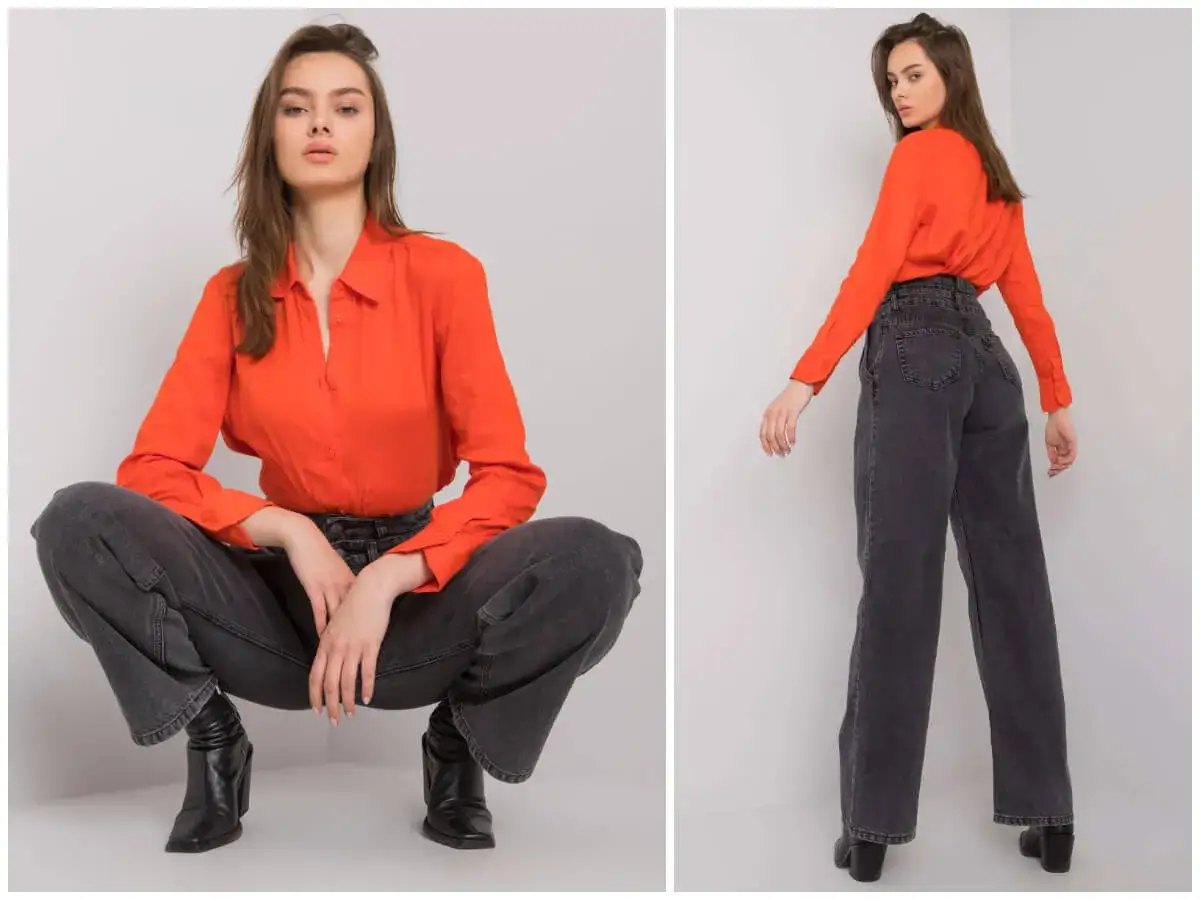 Modelka w pomarańczowej bluzce i ciemnych spodniach wide leg, które podkreślają swobodę i styl.