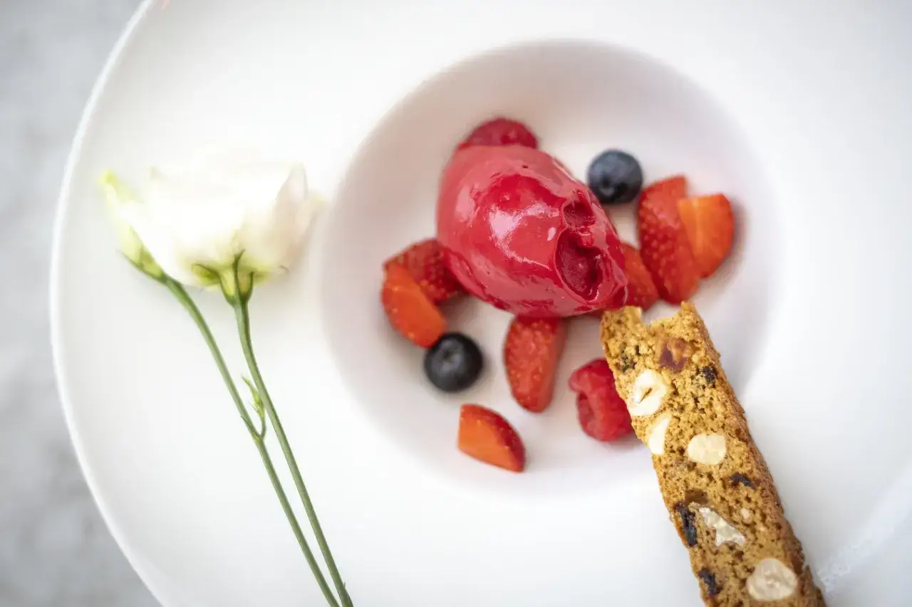 En vacker dessert med hallonsorbet, f&auml;rska b&auml;r och en mandelbiscuits. En vit ros pryder tallriken, som en liten bit av Dalarna.
