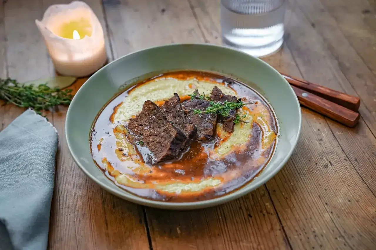 Zartes Brasato al Barolo auf cremigem Polenta, garniert mit frischem Thymian. Ein Fest für die Sinne.