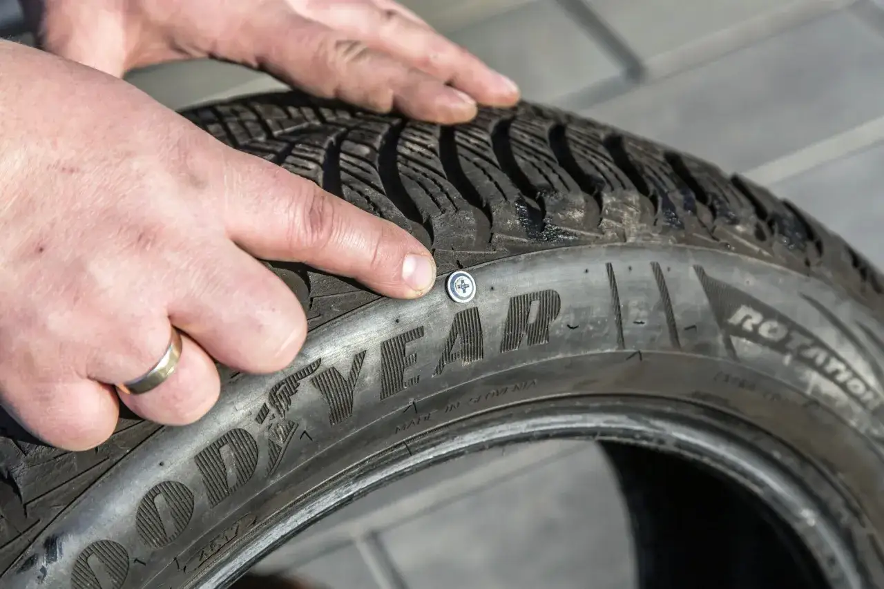 Palec wskazuje śrubę w oponie Goodyear. Widać zużycie bieżnika, co sugeruje, że sparciałe opony mogą być problemem.