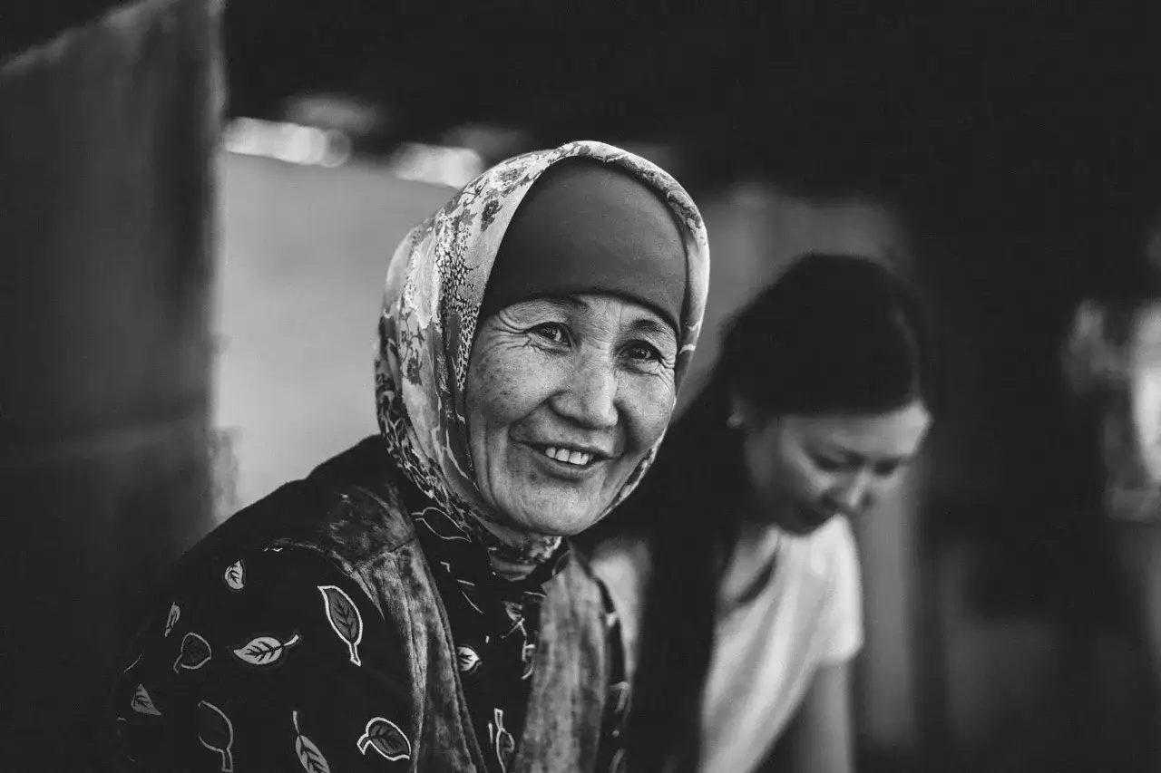 Una anciana sonr&iacute;e, su rostro arrugado cuenta **fotos con historia**. A su lado, una mujer joven se inclina, tambi&eacute;n parte de este relato visual.