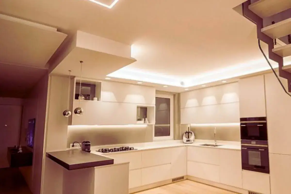 Cucina moderna con controsoffitto a onda illuminato, pensili bianchi e piano snack.