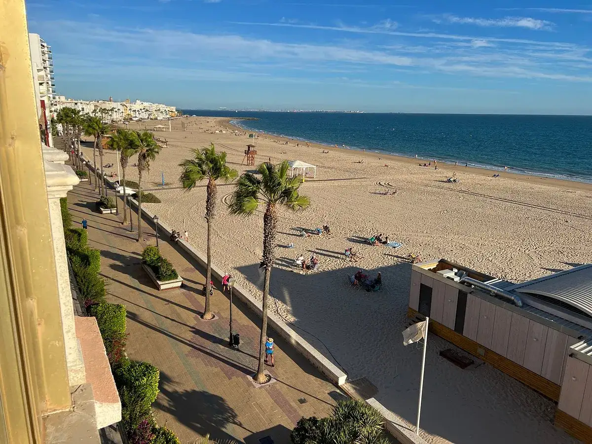 La playa de la Costilla, con palmeras y gente disfrutando del sol y el mar.