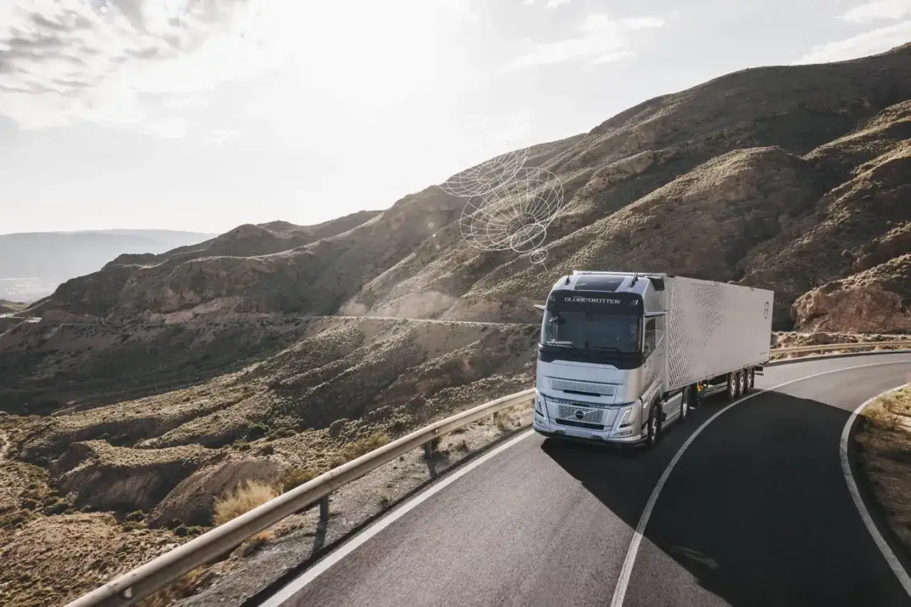Srebrny Volvo FH4 z naczepą jedzie krętą drogą przez górzysty, pustynny krajobraz. Nad kabiną widoczna jest grafika symbolizująca połączenie.