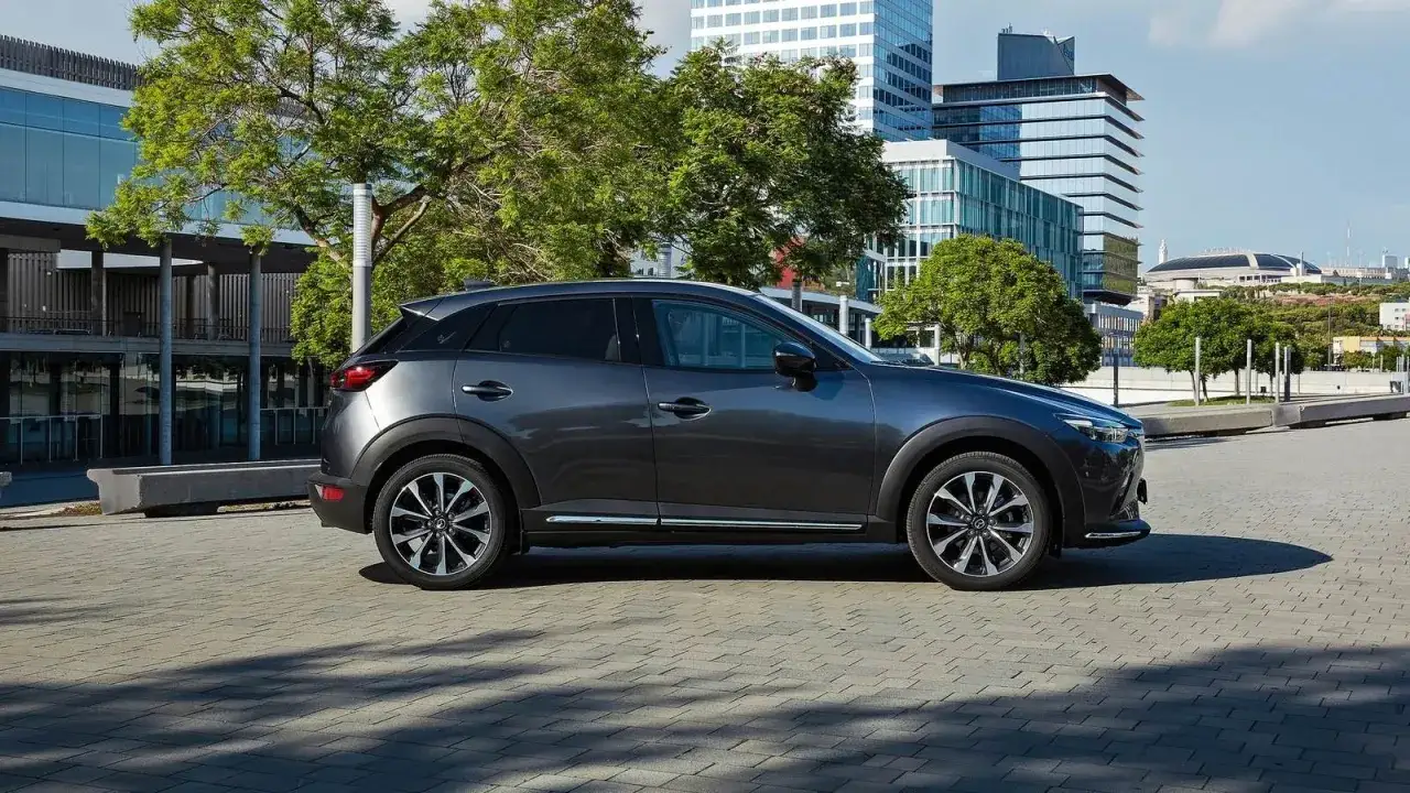 Un Mazda CX-3 gris oscuro estacionado en una zona urbana moderna. Las medidas del Mazda CX-3 son ideales para la ciudad.