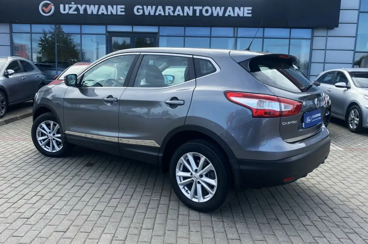 Szary Nissan Qashqai J11 z chromowanymi listwami na progu, zaparkowany przed salonem z napisem 
