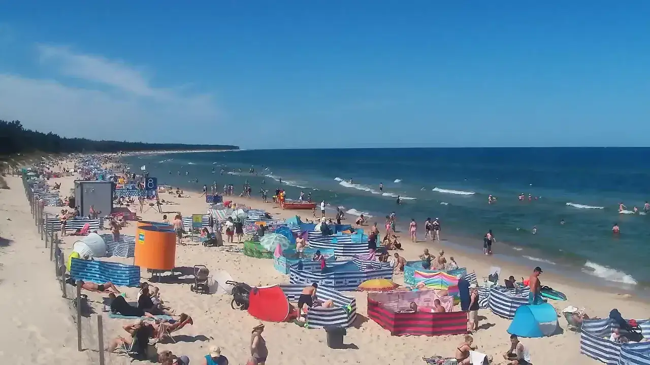 Tłoczny deptak Grzybowo atrakcje: plażowicze, parawany, morze i słońce.