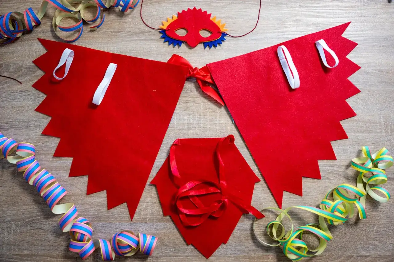Máscara y capa de fieltro rojo para un disfraz pájaro casero, junto a serpentinas de fiesta.
