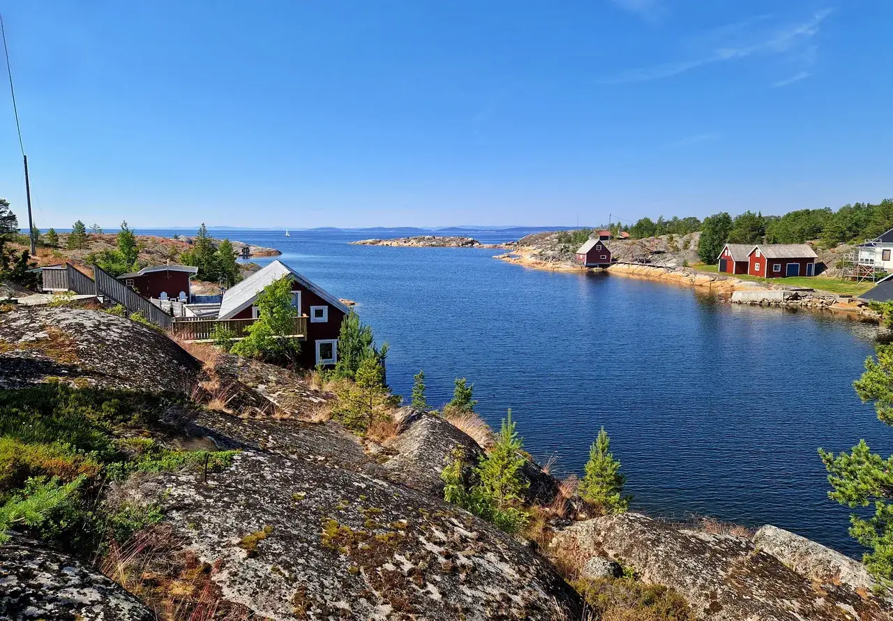 R&ouml;da stugor vid en bl&aring; vik, omgivna av klippor och tr&auml;d. En idyllisk vy som kan vara sveriges finaste strand.