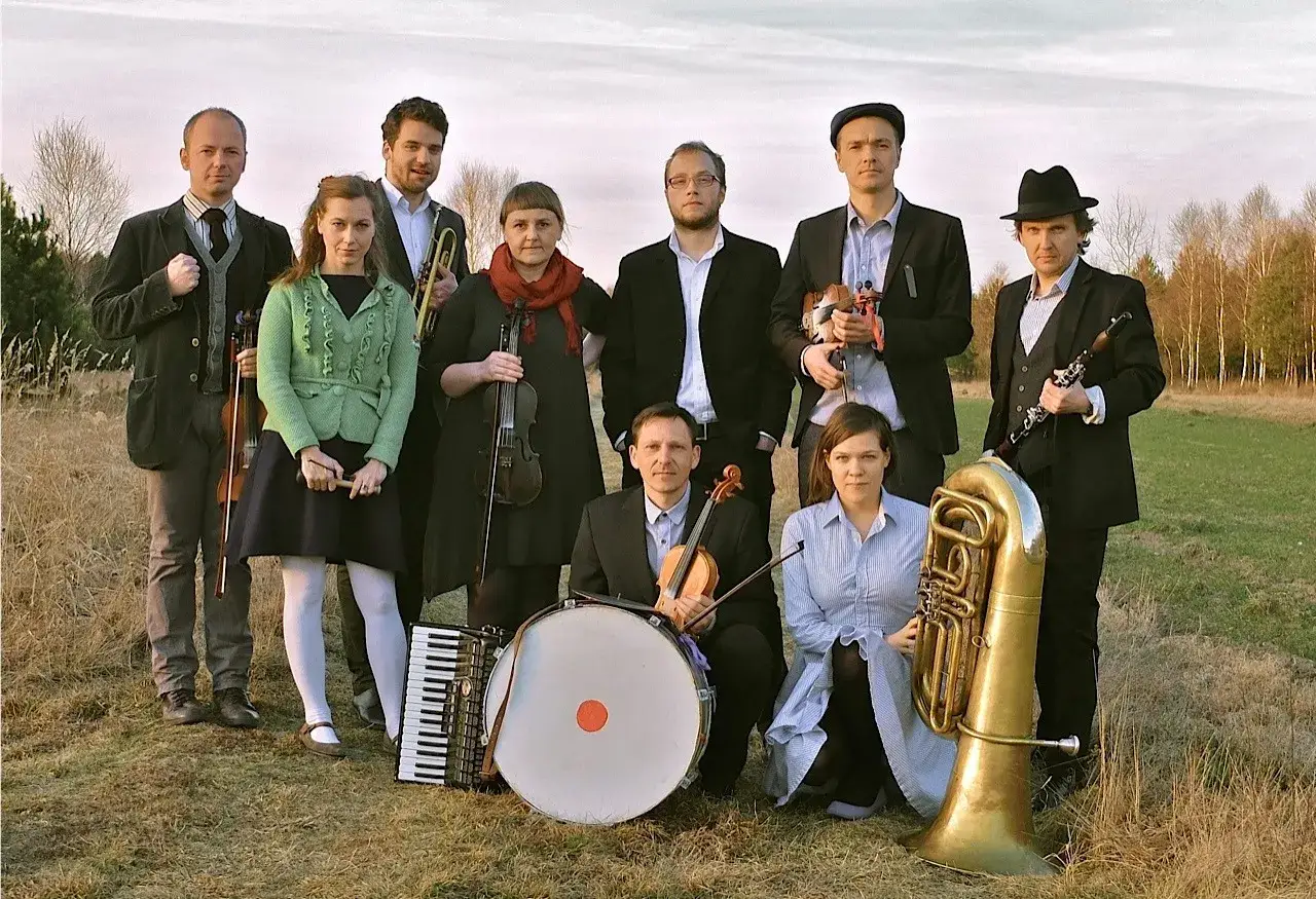 Tęgie chłopy i panie z instrumentami: skrzypce, trąbka, akordeon, bęben, klarnet i tuba.