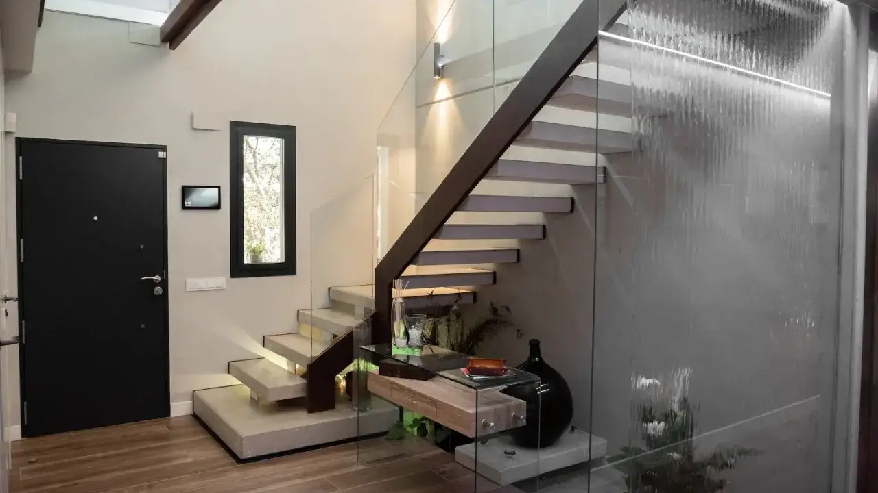 Modernas escaleras interiores prefabricadas con pelda&ntilde;os flotantes de hormig&oacute;n y barandilla de cristal. Una cascada interior ilumina el espacio.