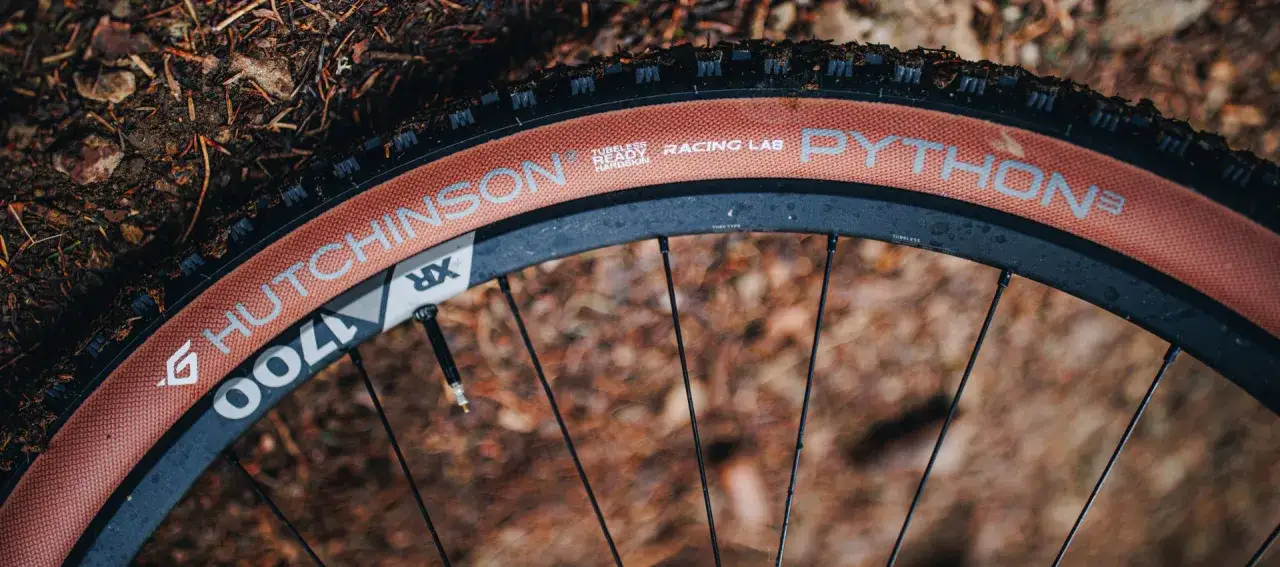 Close-up of a bicycle wheel featuring a Hutchinson Python tire with a tan sidewall, ready for any trail.