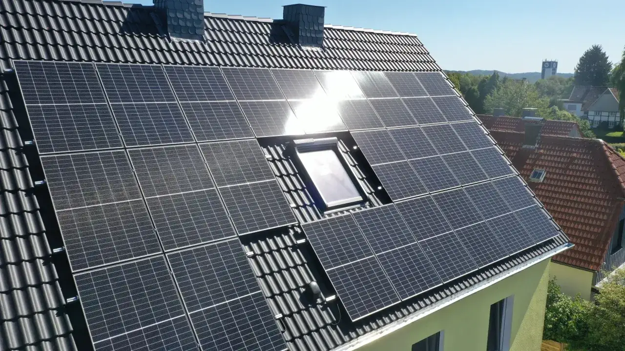 Große Fläche mit **solar aufs dach** Paneelen auf einem dunklen Ziegeldach, daneben ein Dachfenster und Schornsteine.