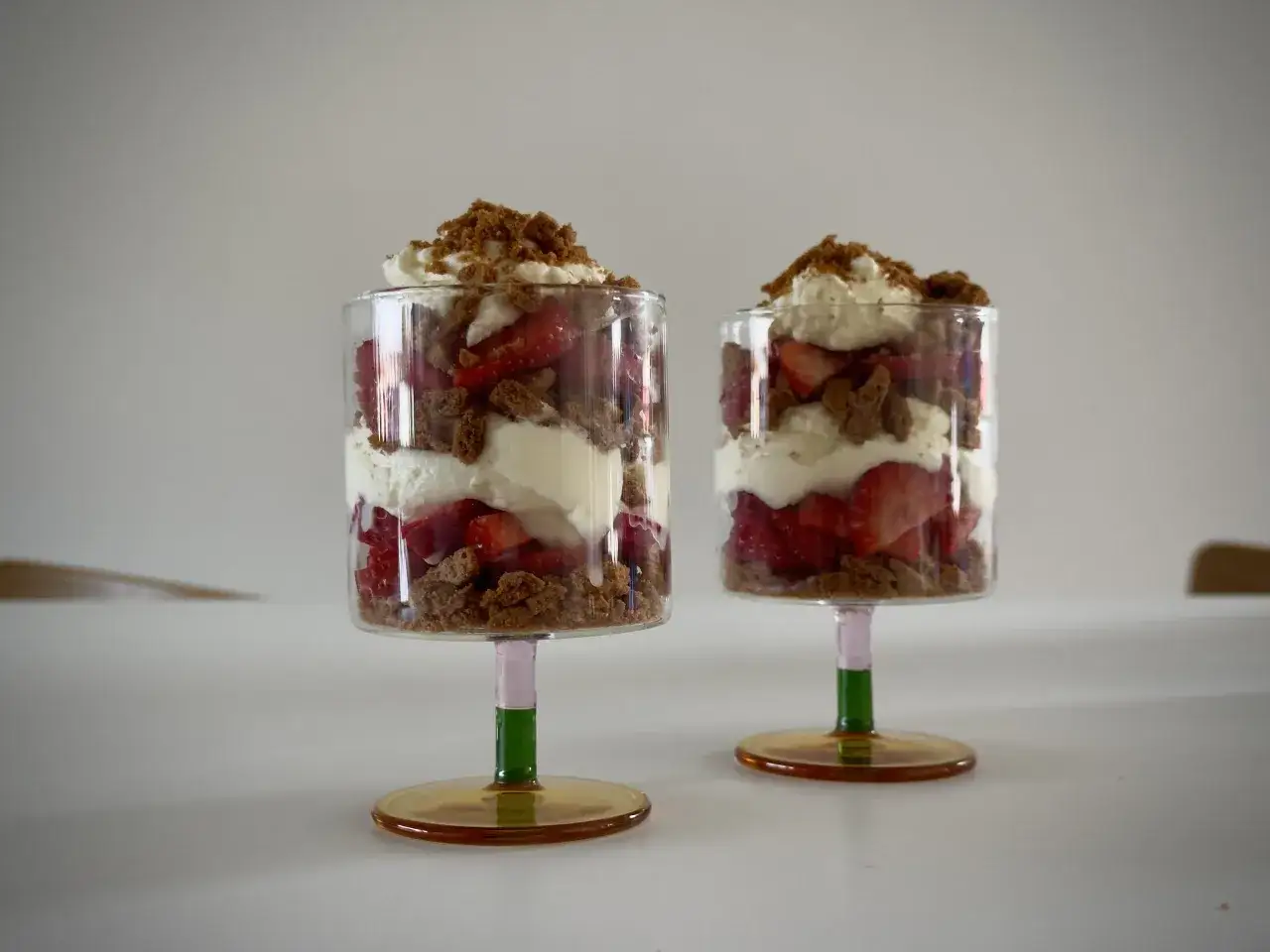 Dwa pucharki z warstwami truskawek, ciasteczek i kremu mascarpone, posypane okruszkami.