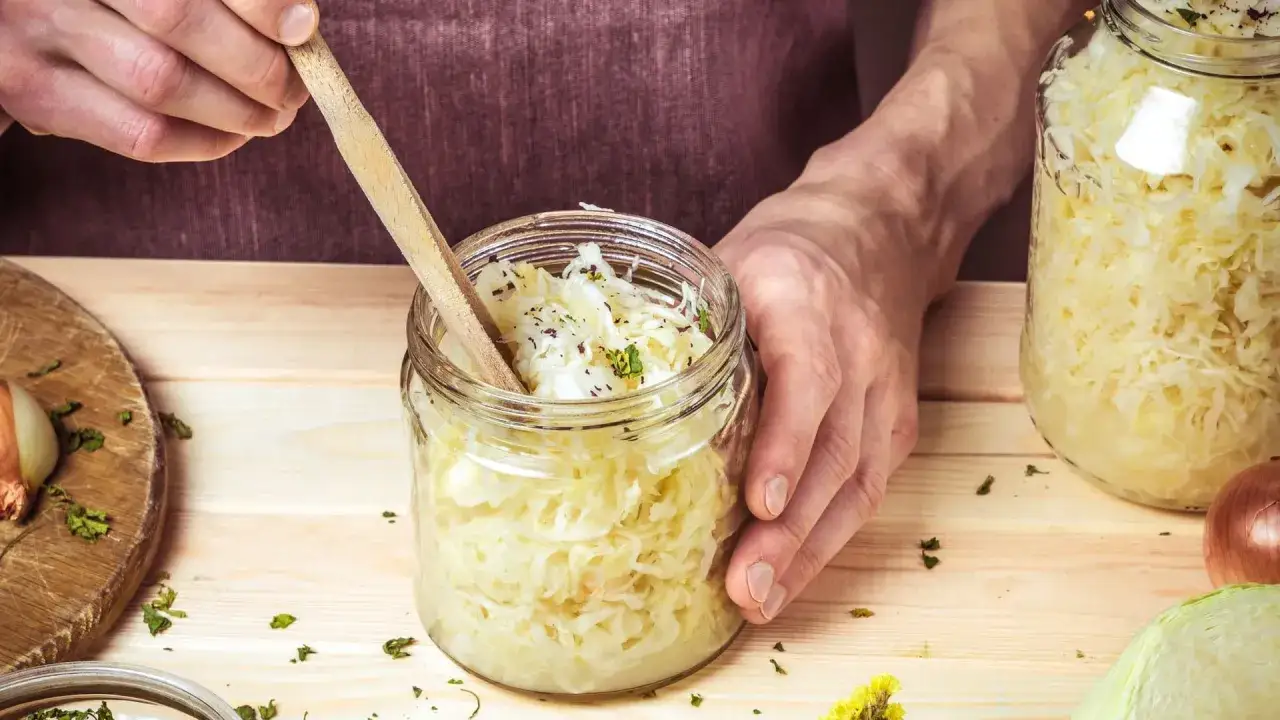 H&auml;nde f&uuml;llen ein Glas mit Sauerkraut. Dieses fermentierte Kraut ist nicht nur lecker, sondern auch sehr gesund.