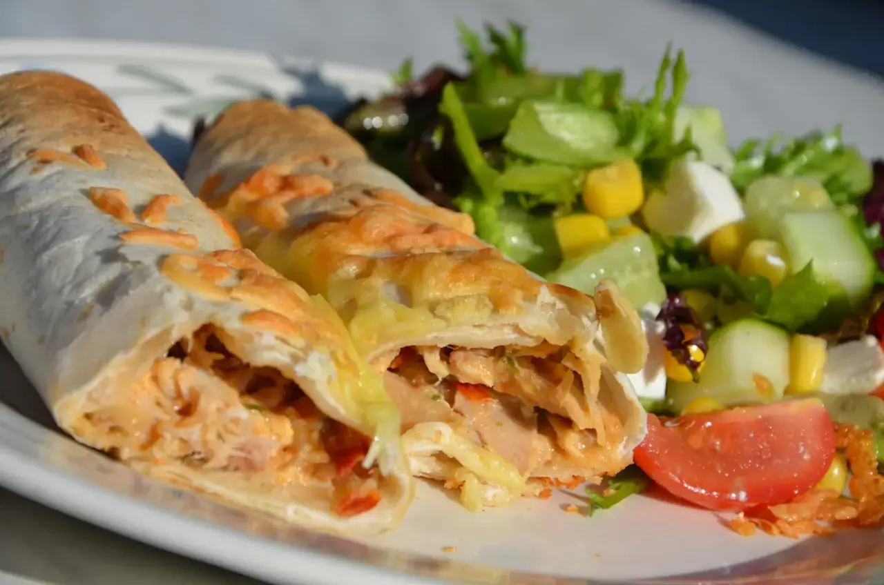 Tv&aring; gyllene enchiladas kyckling med sm&auml;lt ost, serverade med en fr&auml;sch sallad av gurka, majs, fetaost och tomat.