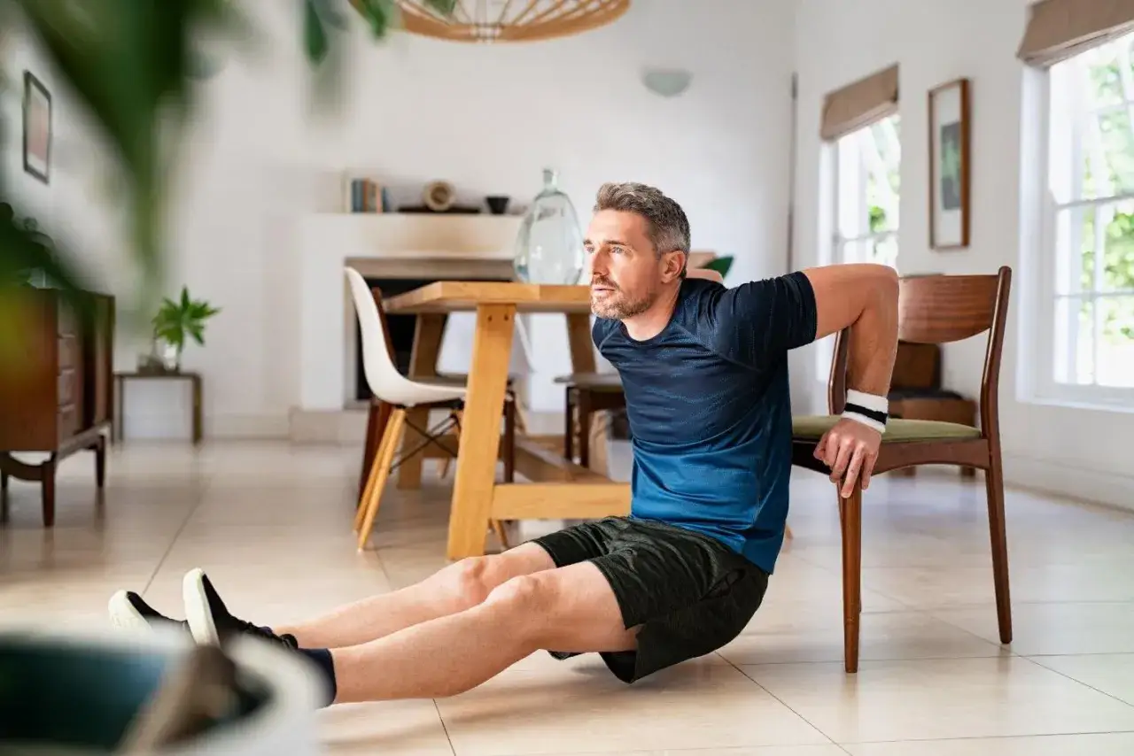 Mann macht Dips auf einem Stuhl zu Hause. So motiviere ich mich zum Sport: Einfach anfangen!