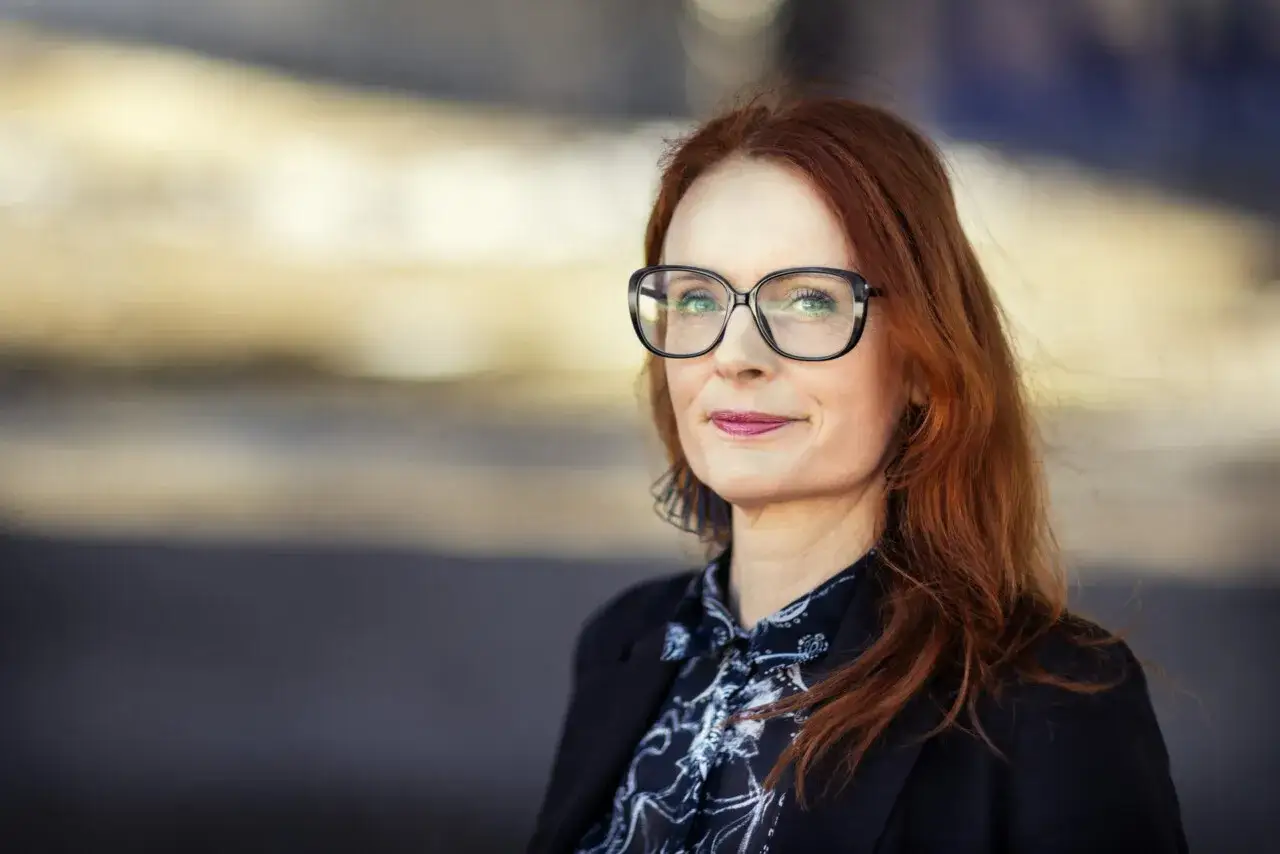 Jenny Aschenbrenner, med sitt röda hår och glasögon, ler mot kameran.