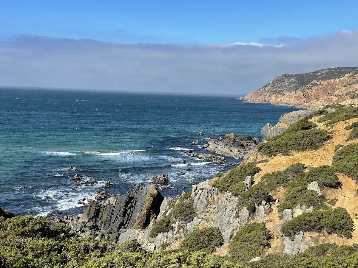 Felsige K&uuml;ste mit t&uuml;rkisfarbenem Meer und gr&uuml;ner Vegetation, ein malerischer Ausblick auf Sintra Cascais.