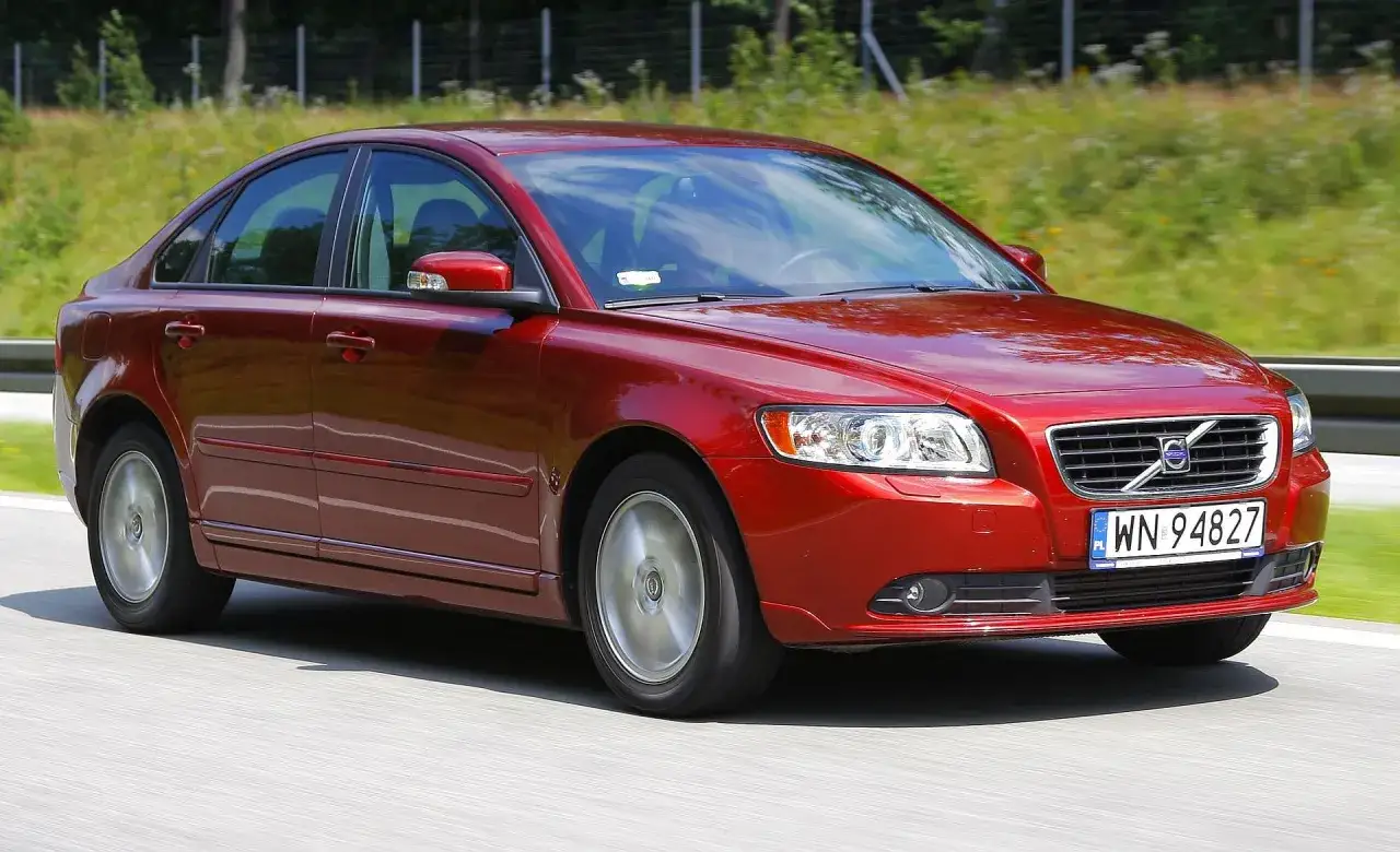 Czerwone Volvo S40 2.0 diesel w ruchu drogowym, z rozmytym tłem zieleni i drogi.