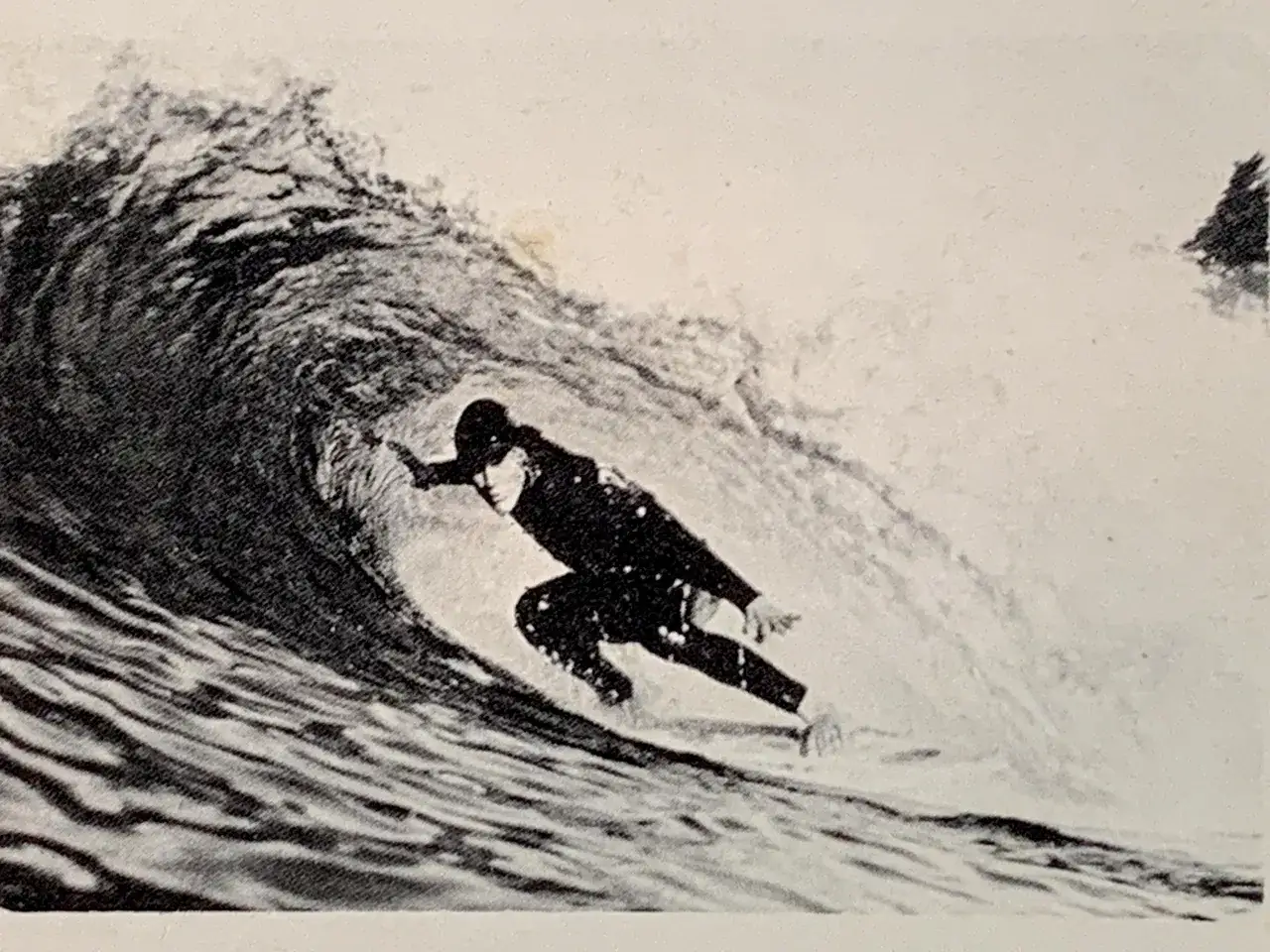 Surfer w czarnym stroju ślizga się po wewnętrznej stronie fali, tworząc tunel wodny.