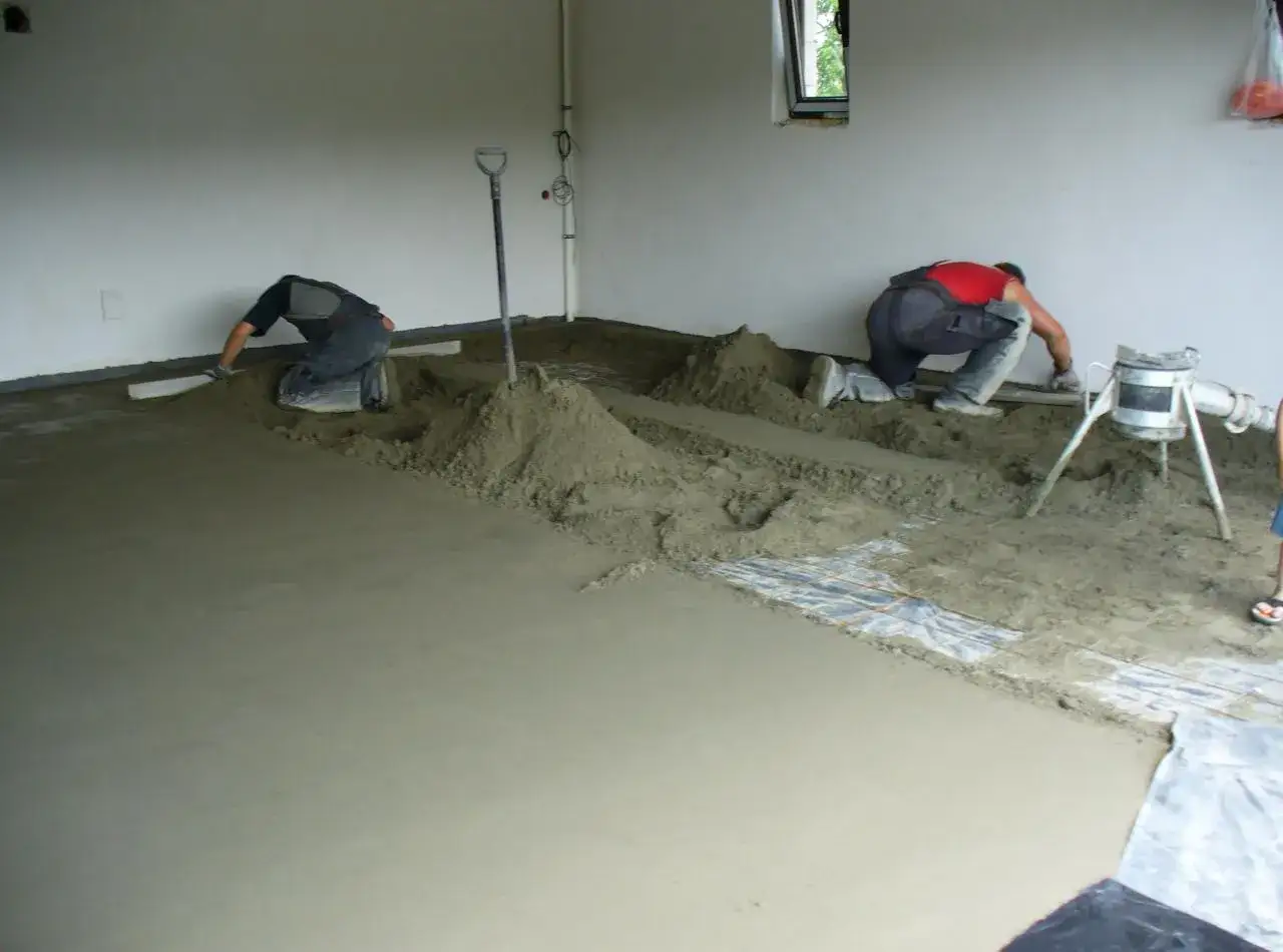 Dwóch robotników wykonuje wylewki miksokretem. Materiał jest rozkładany i wyrównywany.