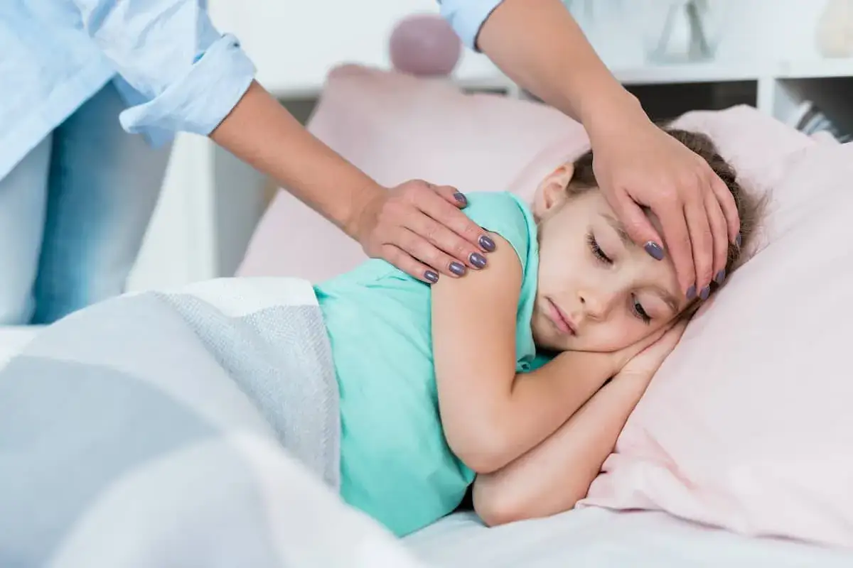 Córka śpi z gorączką, mama kładzie jej rękę na czole. Może potrzebuje smecta dla dzieci?