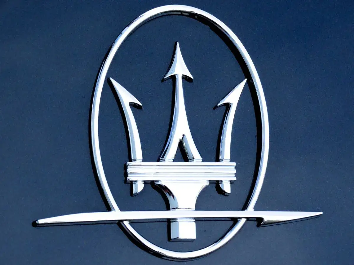 Błyszczący, chromowany tr&oacute;jząb Neptuna - jak wygląda znaczek Maserati na ciemnym tle.