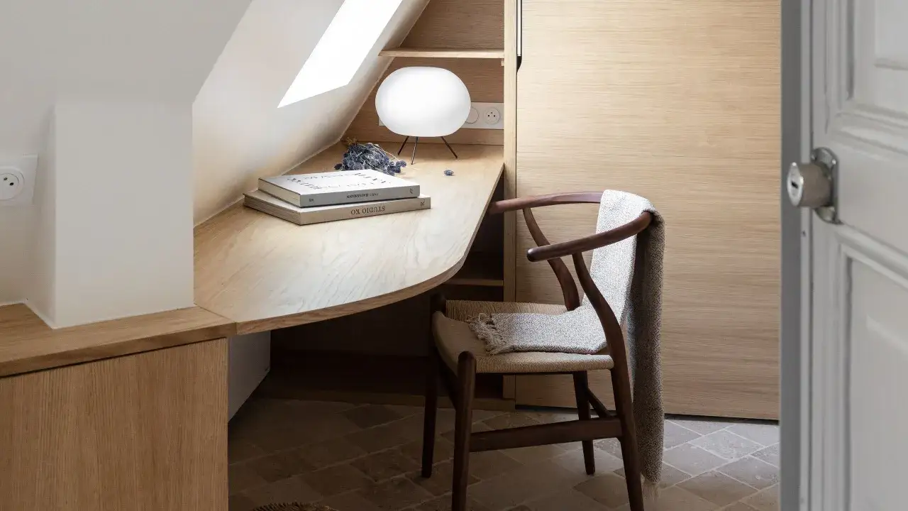 Scrivania in legno con lampada e libri, sedia con plaid. Ottime idee per un ufficio in casa accogliente e funzionale.