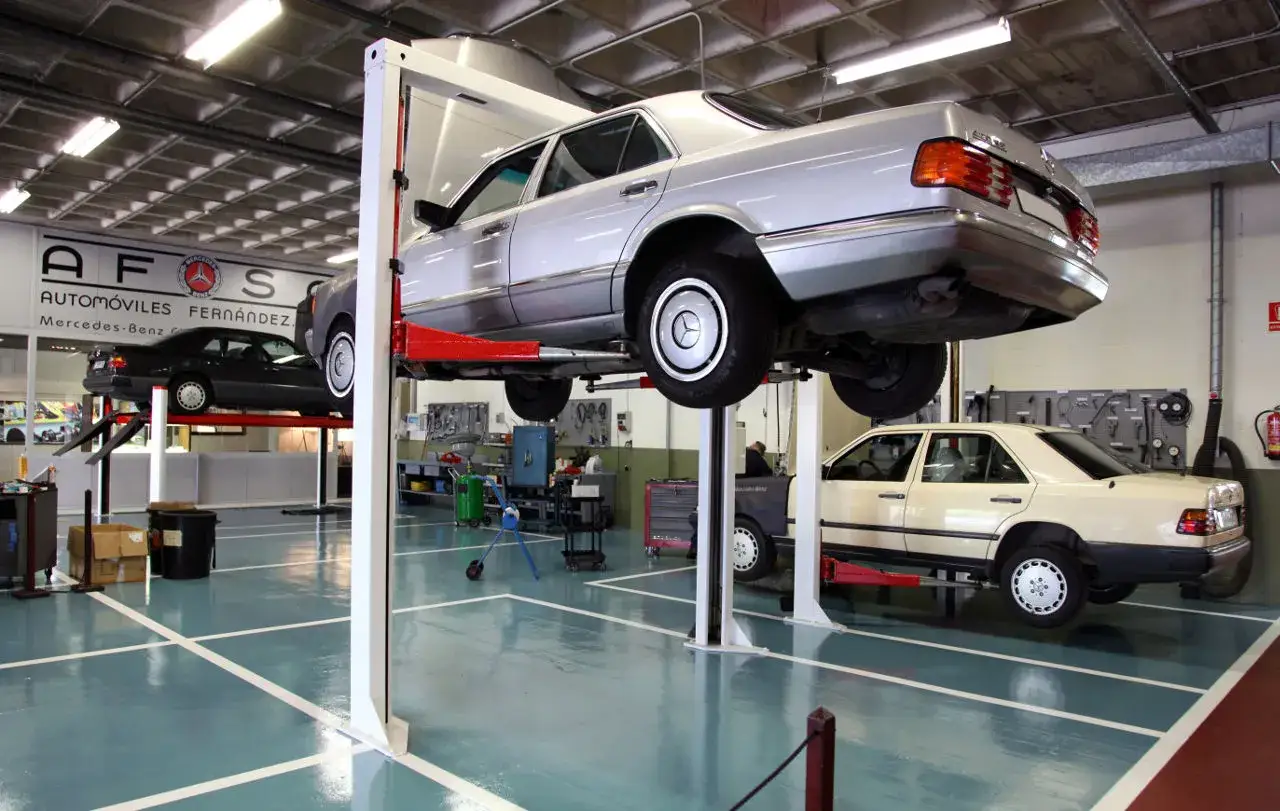 Taller de mantenimiento a de Mercedes-Benz. Dos coches cl&aacute;sicos en elevadores, uno plateado y otro beige, listos para su revisi&oacute;n.
