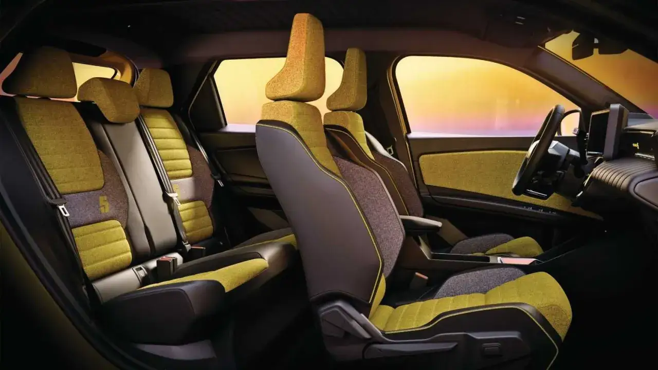 Wnętrze renault 5 electric z żółto-szarymi siedzeniami i widokiem na zachód słońca.
