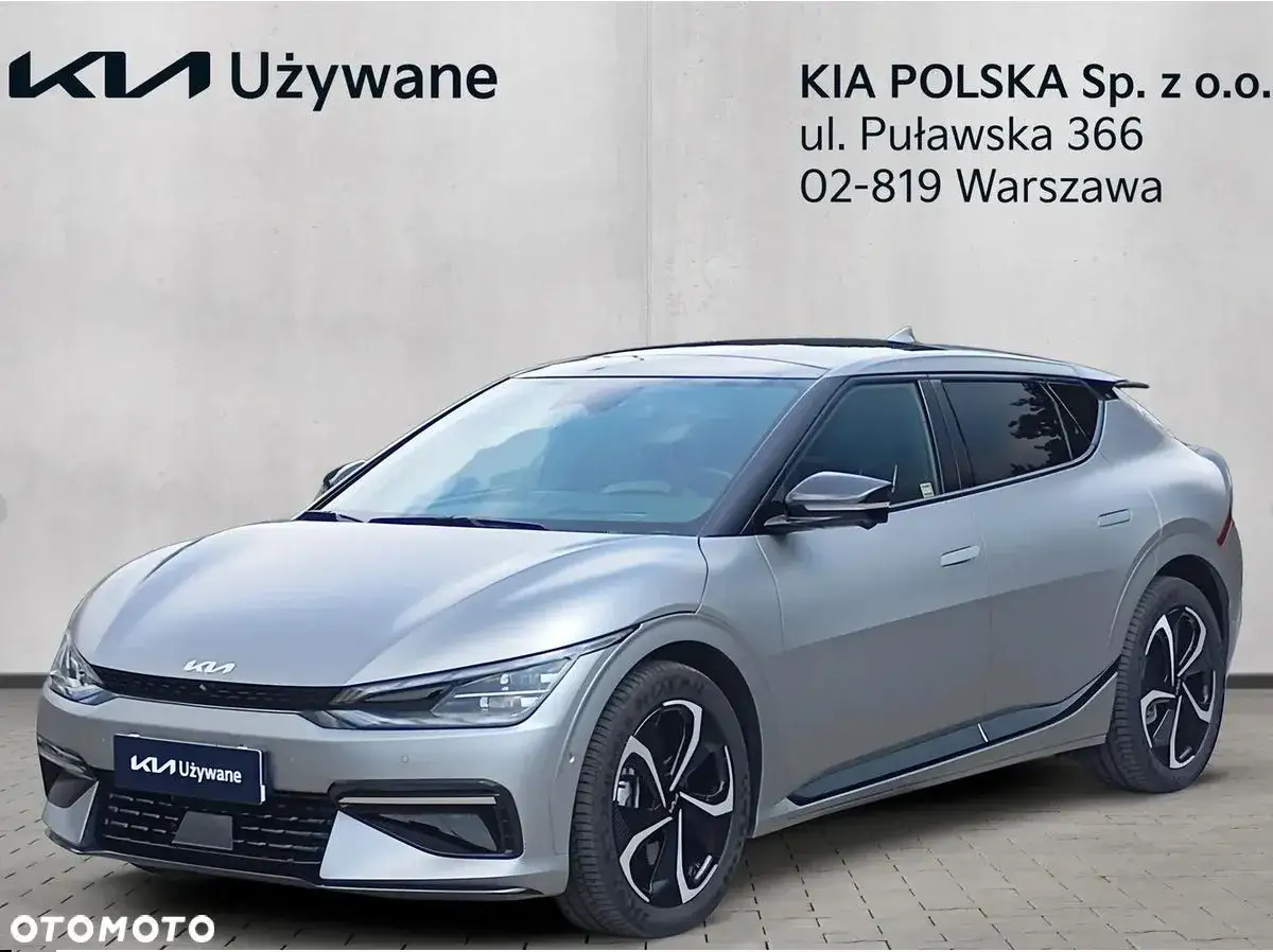 Srebrne Kia EV6 na tle ściany z logo Kia Używane. Idealne do miejskiego testu.
