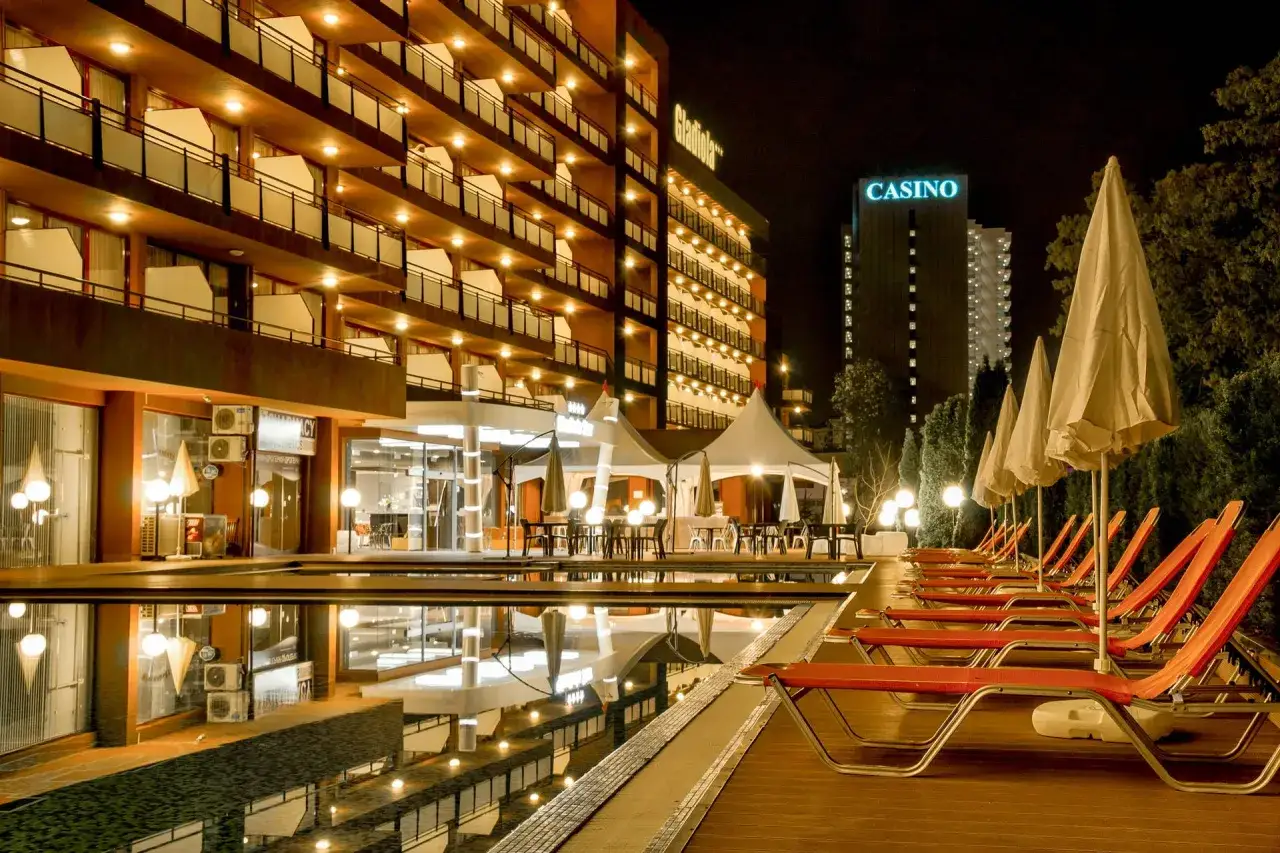 Hotel Gladiola nocą, z basenem i rzędem leżaków. W tle budynek z napisem CASINO.