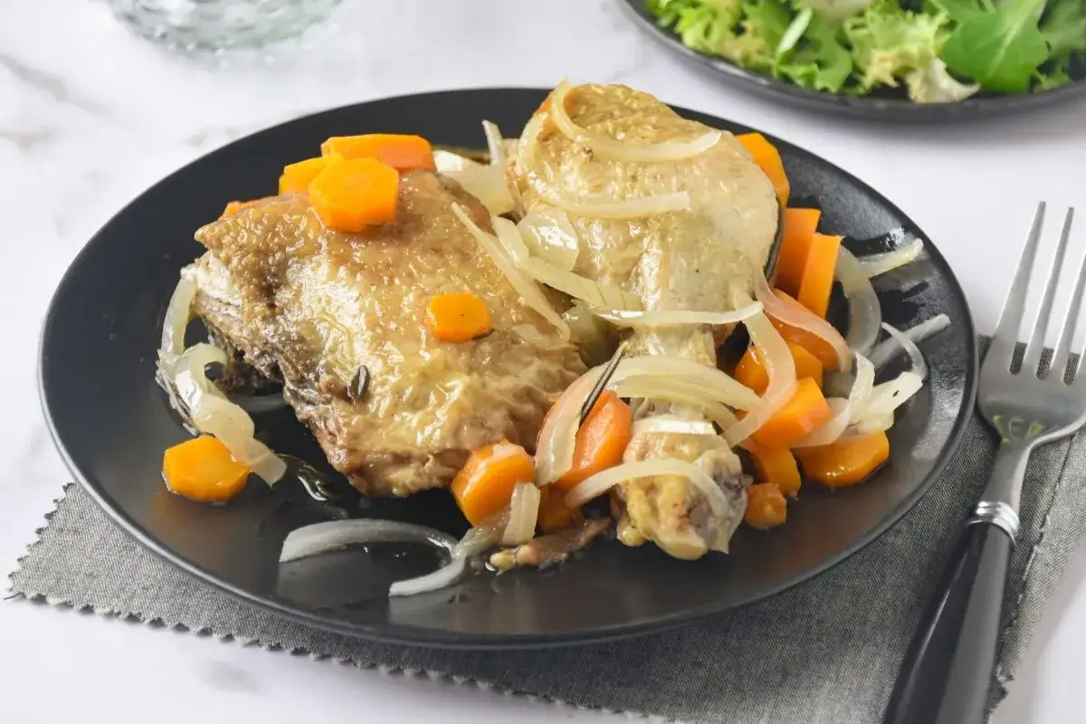 Pechuga de pollo en escabeche con zanahorias y cebolla, servida en plato negro con tenedor.