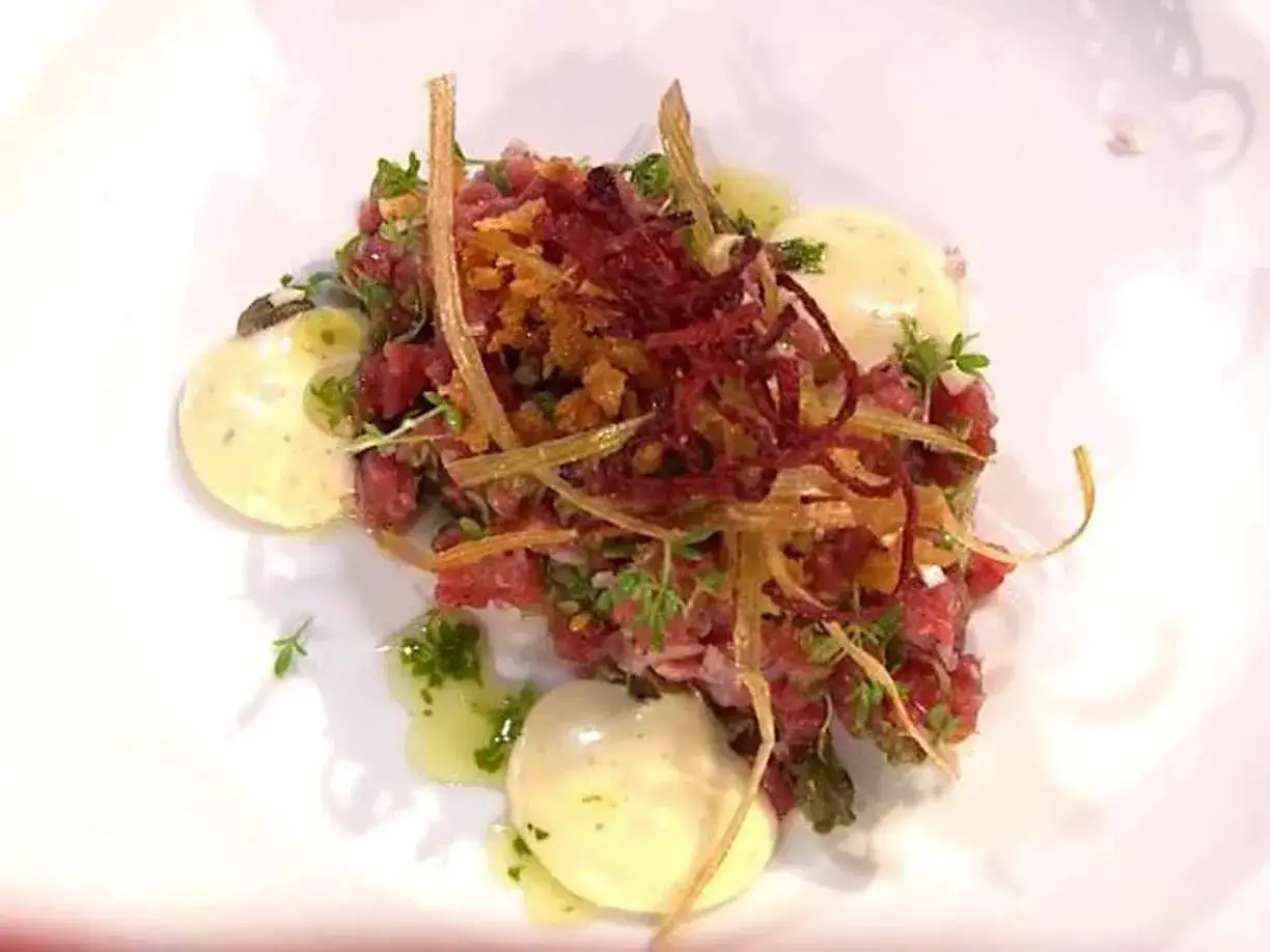 En konstn&auml;rlig tallrik med carne cruda, toppad med krispiga rotfrukter och &ouml;rter, serverad med kr&auml;miga &auml;ggulor.