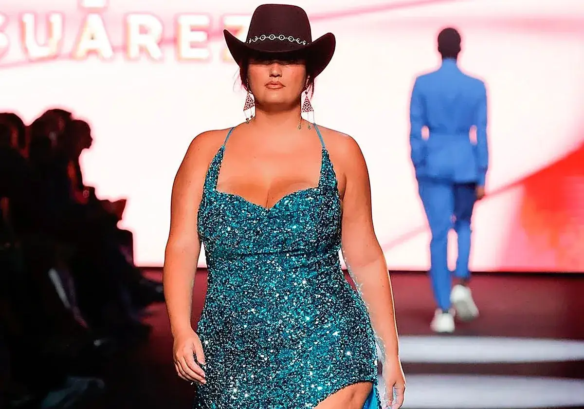 Modelo curvy desfila con un vestido brillante y sombrero vaquero.