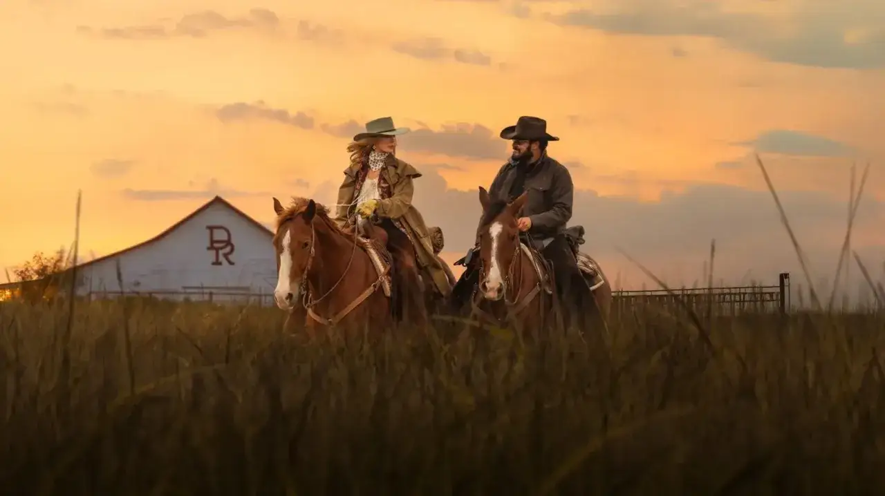Deux cavaliers traversent un champ au coucher du soleil, devant une grange. Un aperçu du yellowstone saison 5 résumé.
