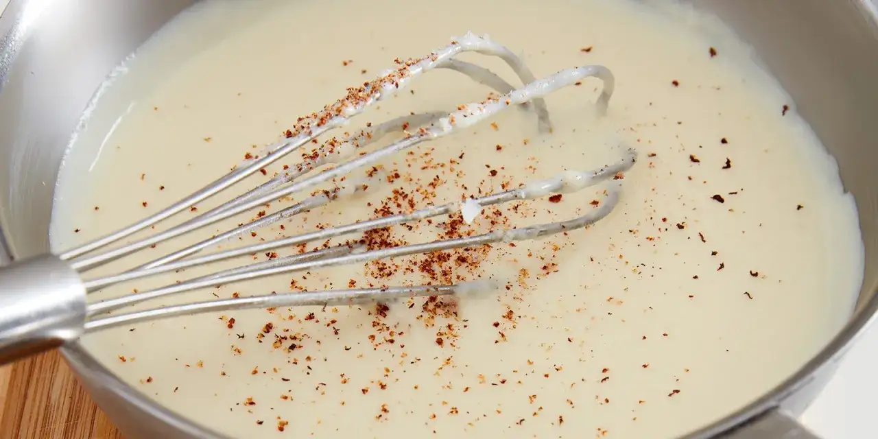 En visp med bechamelsås recept i en kastrull, strödd med peppar.