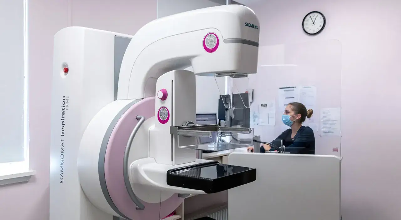 Ein modernes 3D-Mammographie-Ger&auml;t von Siemens steht bereit. Eine medizinische Fachkraft mit Maske sitzt im Hintergrund.