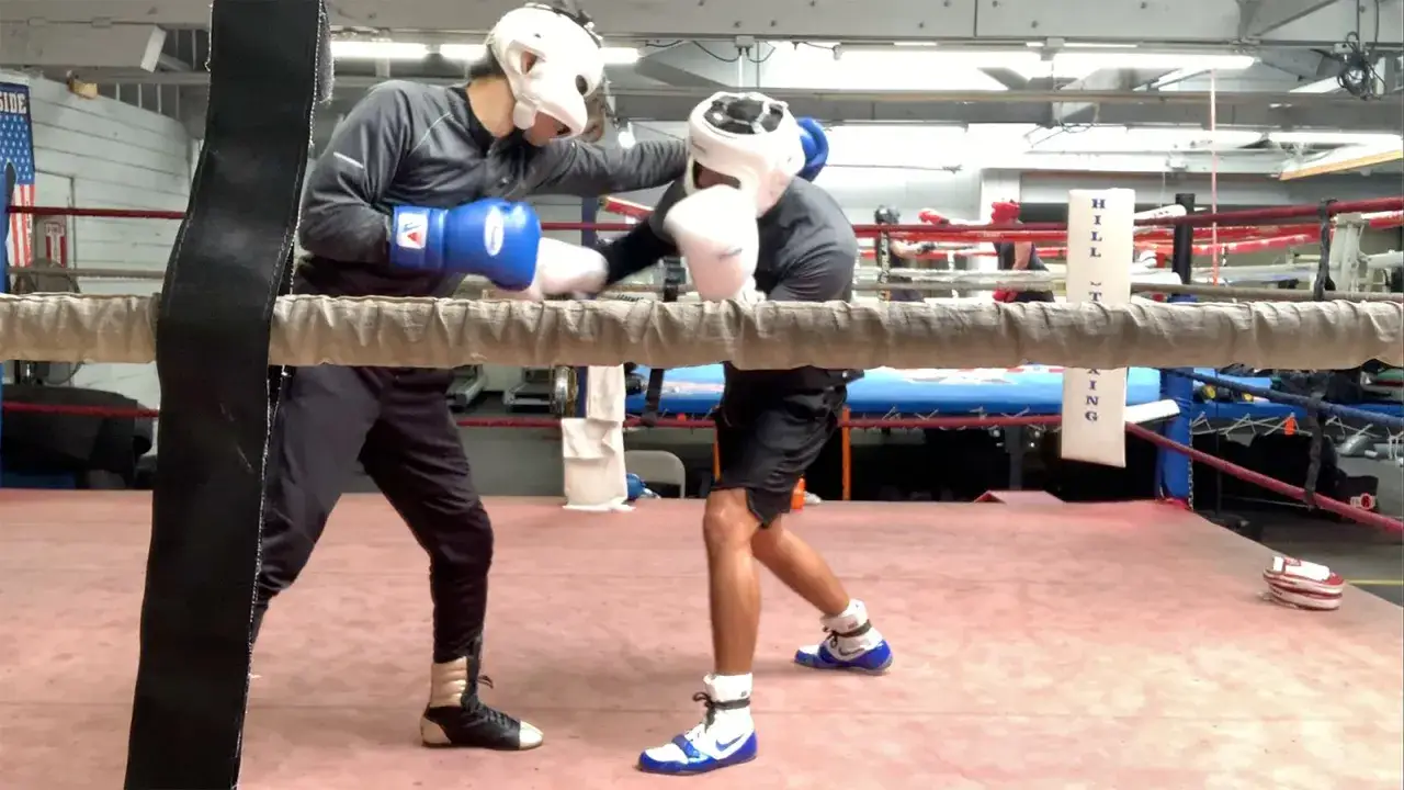 Two boxers practice boxing combos with slips in a gym. One boxer throws a punch while the other dodges.