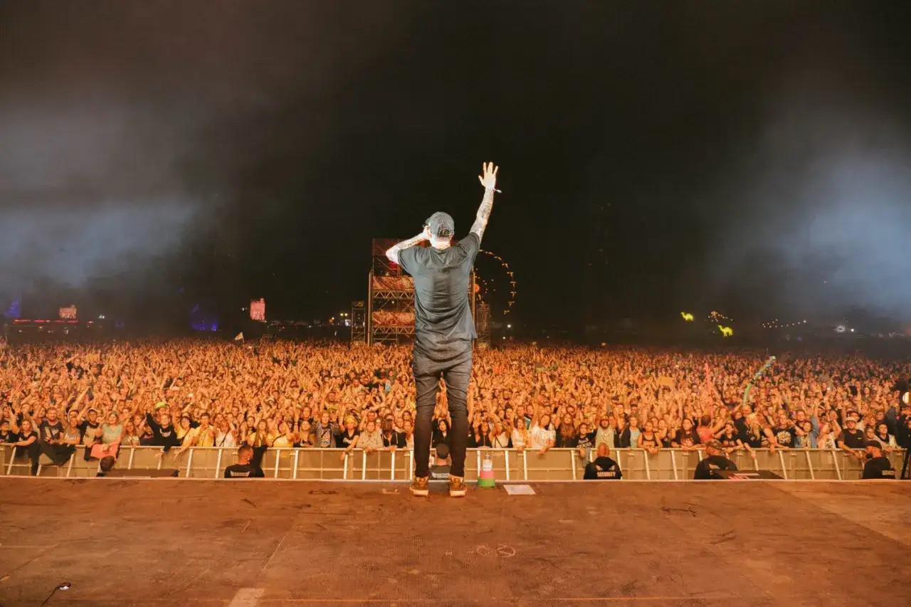Bekannter Rapper winkt einer riesigen Menge zu, die bei einem Konzert jubelt.